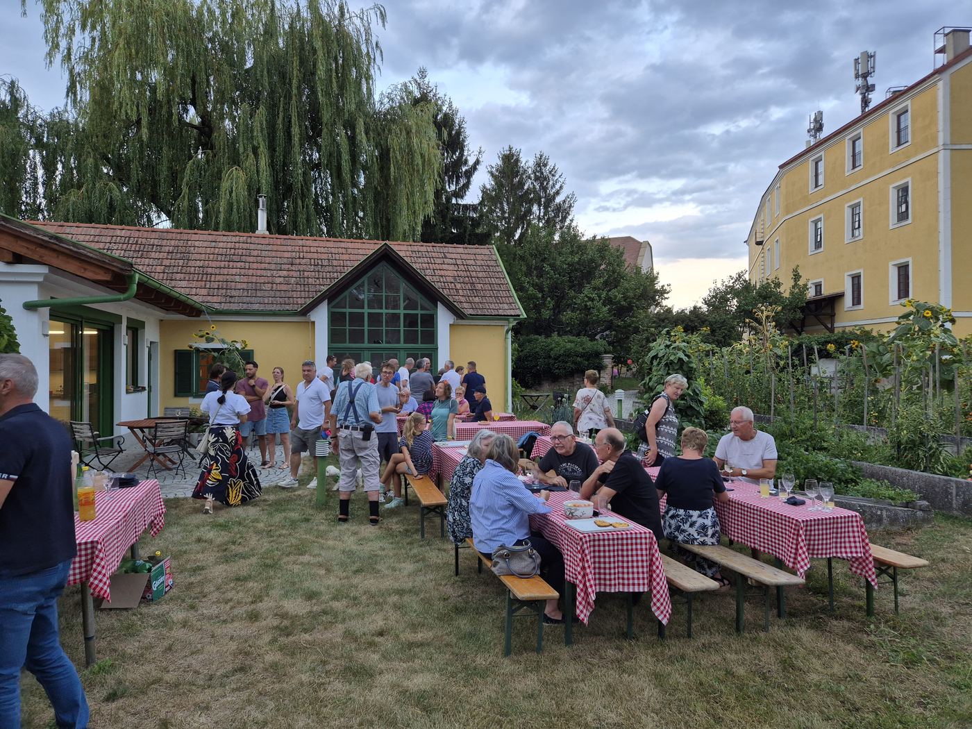 Gäste des Open House sitzen an langen Tischen im Garten und unterhalten sich
